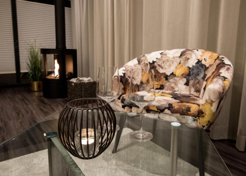 Salon d’une péniche à Offingawier avec fauteuil fleuri, table en verre, verres à vin et cheminée.