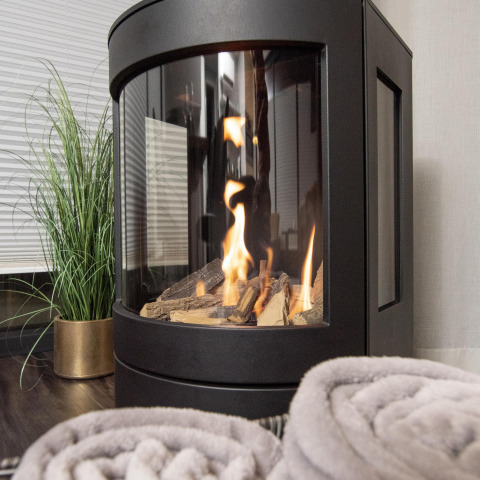 Moderne pejs med flammer og træstykker, tæpper og grøn plante på husbåd i Offingawier, Friesland.