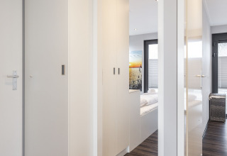 Interior luminoso de una casa flotante con suelo de madera y armarios blancos, acceso al dormitorio en Friesland.