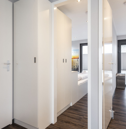 Interior luminoso de una casa flotante con suelo de madera y armarios blancos, acceso al dormitorio en Friesland.