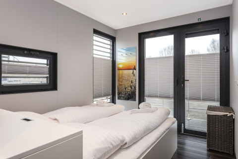 Chambre moderne sur une péniche avec lit double, grandes fenêtres et tableau de coucher de soleil mural.