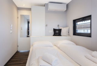 Moderne, lys bådhytte med dobbeltseng, vindue, aircondition og håndklæder på sengen i Friesland.