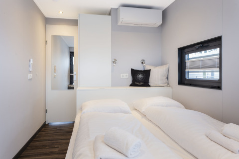 Moderne, heldere kamer op woonboot met tweepersoonsbed, raam, airco en handdoeken op bed in Friesland.