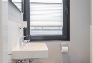Moderne badeværelse med hvid vask, vindue med persienne og toilet på en husbåd i Offingawier, Friesland.