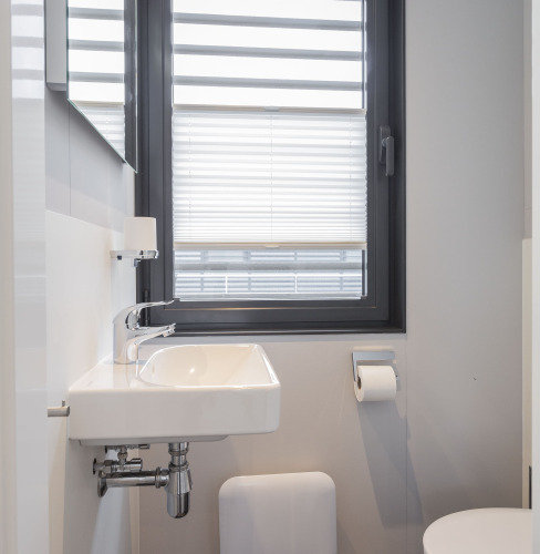 Baño moderno con lavabo blanco, persiana de ventana y WC en una casa flotante en Offingawier, Frisia.