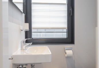 Moderne badkamer met witte wastafel, jaloezieën en toilet op een woonboot in Offingawier, Friesland.