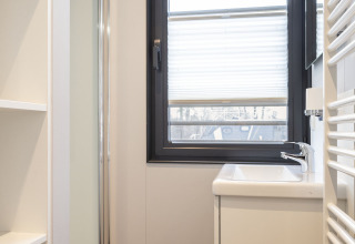 Lichte, moderne badkamer op een woonboot in Offingawier met raam, wastafel en witte planken.
