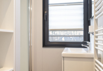 Baño moderno y luminoso en una casa flotante en Offingawier, con ventana, lavabo y estanterías blancas.