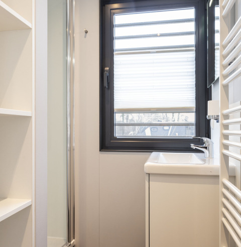 Lichte, moderne badkamer op een woonboot in Offingawier met raam, wastafel en witte planken.