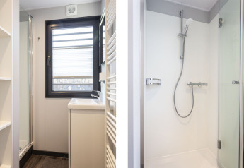 Salle de bain moderne sur une péniche à Offingawier, avec douche, lavabo et grande fenêtre lumineuse.