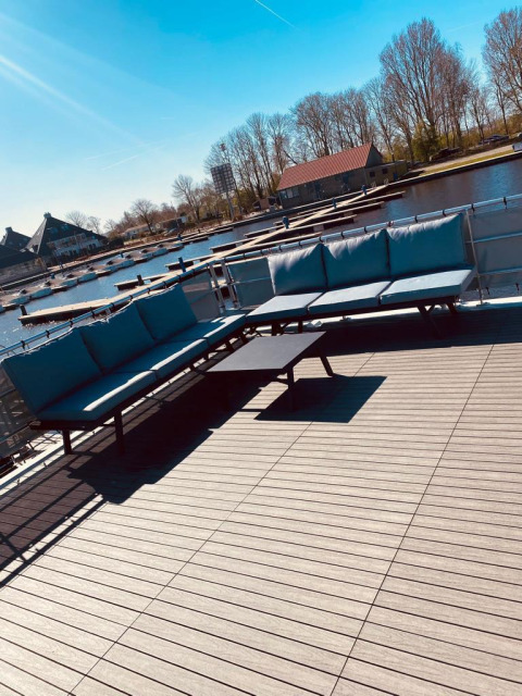 Udendørs terrasse på en husbåd i Offingawier, Friesland med sofaer og udsigt over kanalen i solskin.