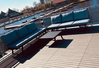 Terraza en la azotea de una casa flotante en Offingawier, Frisia, con sofás y vista al canal al sol.