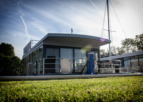 Casa flotante moderna con terraza en la azotea en Offingawier, Países Bajos, vista desde el césped al sol.