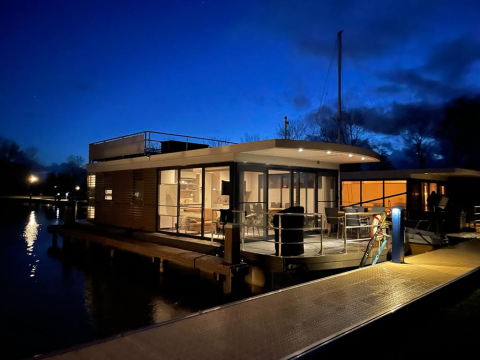 Foto nocturna de una casa flotante con terraza en Offingawier, Frisia, iluminada bajo el cielo azul oscuro.