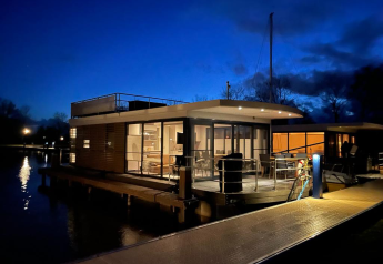 Foto nocturna de una casa flotante con terraza en Offingawier, Frisia, iluminada bajo el cielo azul oscuro.