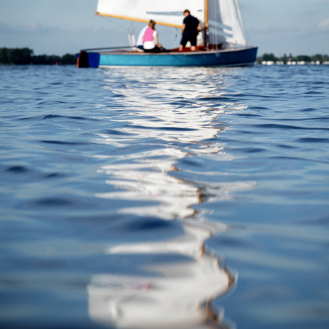 Fokus auf die Wasseroberfläche, unscharfes Segelboot mit zwei Personen im Hintergrund, Offingawier, Friesland.