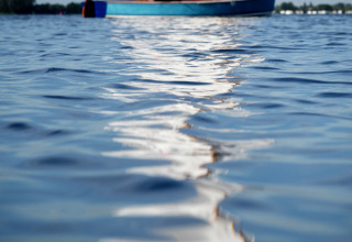 Enfoque en la superficie del agua con un barco de vela desenfocado y dos personas al fondo, Offingawier, Frisia.