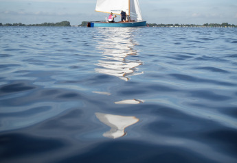 Barca a vela sull’acqua calma vicino a Offingawier, Houseboat + terrazza, Friesland, Paesi Bassi, cielo sereno.
