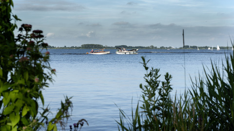Vista al lago y botes desde una casa flotante con terraza en Offingawier, Frisia, Países Bajos, enmarcada por plantas.