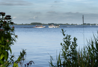 Vista sul lago e sulle barche da una casa galleggiante con terrazza a Offingawier, Frisia, Paesi Bassi, tra le piante.