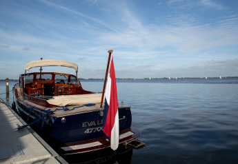 Péniche avec terrasse sur le toit amarrée à un quai, eau calme et drapeau néerlandais, Offingawier, Friesland.