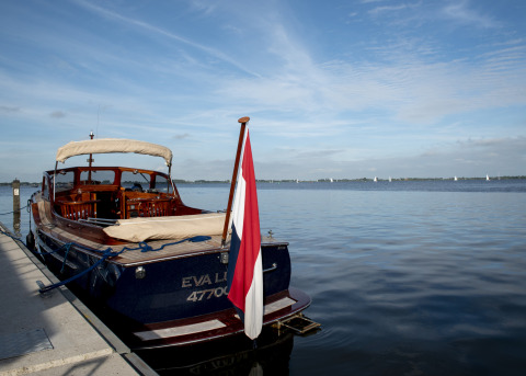 Woonboot met dakterras aangemeerd aan een steiger, kalm water en Nederlandse vlag, Offingawier, Friesland.