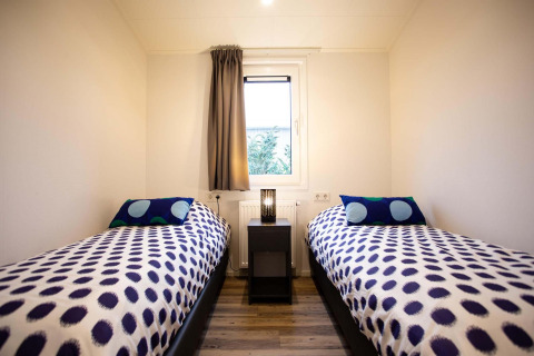 Habitación moderna con dos camas individuales, colchas de lunares, ventana en Nature Lodge Wellness.