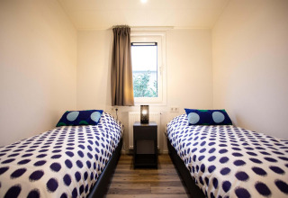 Habitación moderna con dos camas individuales, colchas de lunares, ventana en Nature Lodge Wellness.