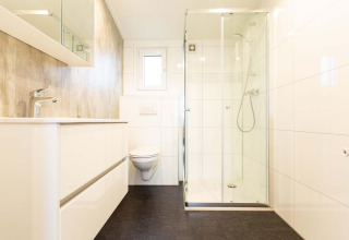 Moderne, rummeligt badeværelse med brusekabine og væghængt toilet i Nature Lodge Wellness, Park Westerkogge.