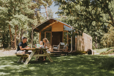 Familie beim Picknick vor einer modernen Wikkelhouse-Lodge im Beerze Bulten, Niederlande, im Grünen.