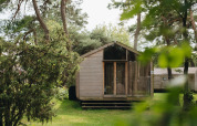 Voorzijde van de Wikkelhouse lodge bij Beerze Bulten in Nederland, omringd door bomen en groen gras.