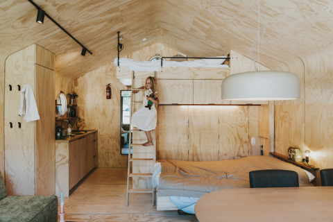 Interior de la cabaña Wikkelhouse en Beerze Bulten, Países Bajos, con cama alta y niña pequeña en escalera.