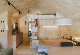 Interior de la cabaña Wikkelhouse en Beerze Bulten, Países Bajos, con cama alta y niña pequeña en escalera.