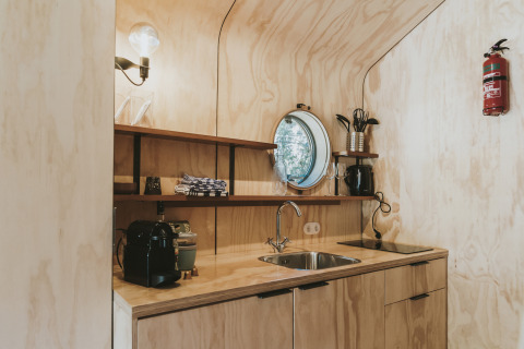 Cocina moderna y compacta en Wikkelhouse, Beerze Bulten, Países Bajos, con paneles de madera y ventana circular.
