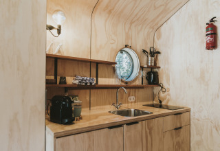 Cocina moderna y compacta en Wikkelhouse, Beerze Bulten, Países Bajos, con paneles de madera y ventana circular.