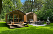 Dos cabañas modernas de madera con terrazas en Wikkelhouse Duo, Beerze Bulten, Países Bajos, rodeadas de naturaleza.
