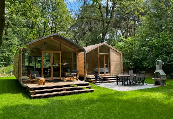 Twee moderne houten huisjes met terrassen bij Wikkelhouse Duo, Beerze Bulten, Nederland, tussen het groen.