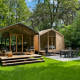 Twee moderne houten huisjes met terrassen bij Wikkelhouse Duo, Beerze Bulten, Nederland, tussen het groen.
