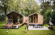 Familie leger foran Wikkelhouse Duo lodge på Beerze Bulten, omringet af træer i Holland.