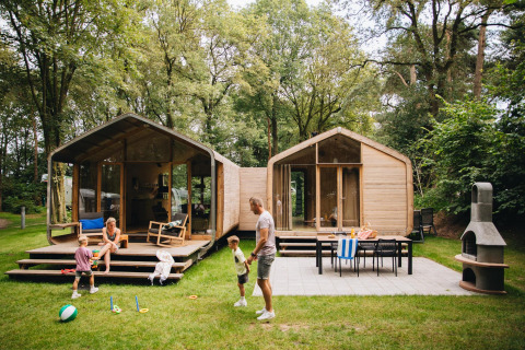 Famiglia che gioca davanti al Wikkelhouse Duo lodge a Beerze Bulten, circondata da alberi nei Paesi Bassi.