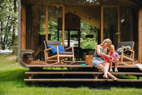 Moeder en kind zitten op de trappen van hun Wikkelhouse Duo lodge in Beerze Bulten, Nederland.