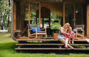 Moeder en kind zitten op de trappen van hun Wikkelhouse Duo lodge in Beerze Bulten, Nederland.