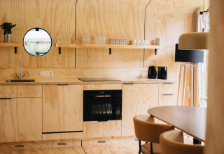 Licht houten lodgekeuken met ronde spiegel, open rekken en eethoek in Wikkelhouse Duo, Beerze Bulten.