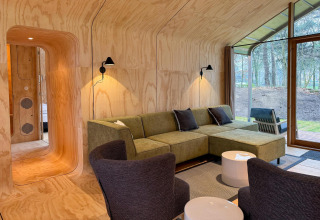 Moderne lodge woonkamer met houten panelen, groene bank en grote ramen in Wikkelhouse Duo, Beerze Bulten.