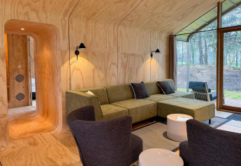 Moderne lodge woonkamer met houten panelen, groene bank en grote ramen in Wikkelhouse Duo, Beerze Bulten.