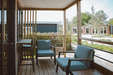 Knusse veranda met stoelen bij de Tiny Court lodge in vakantiepark De Boshoek, Nederland, met uitzicht op groen.