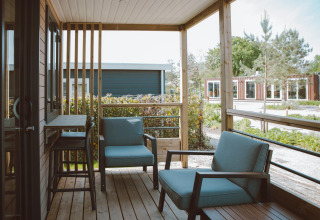 Porche acogedor con sillones en la lodge Tiny Court del parque vacacional De Boshoek, Países Bajos, con jardines.