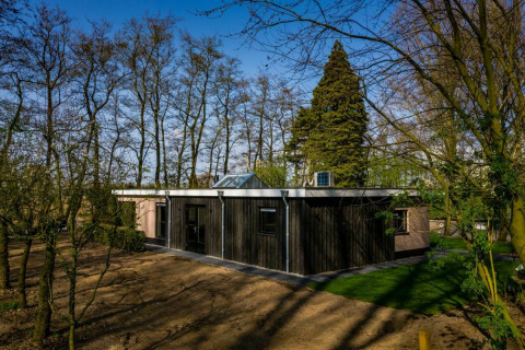 Casa de campo en Buitengoed Ruysbos, Países Bajos, rodeada de árboles y naturaleza, cielo despejado.