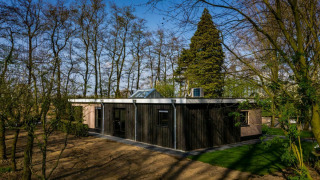 Lodge ved Buitengoed Ruysbos i Holland, omgivet af træer og natur, set under blå himmel.