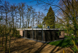 Lodge im Buitengoed Ruysbos, Niederlande, umgeben von Bäumen und Natur, unter blauem Himmel.